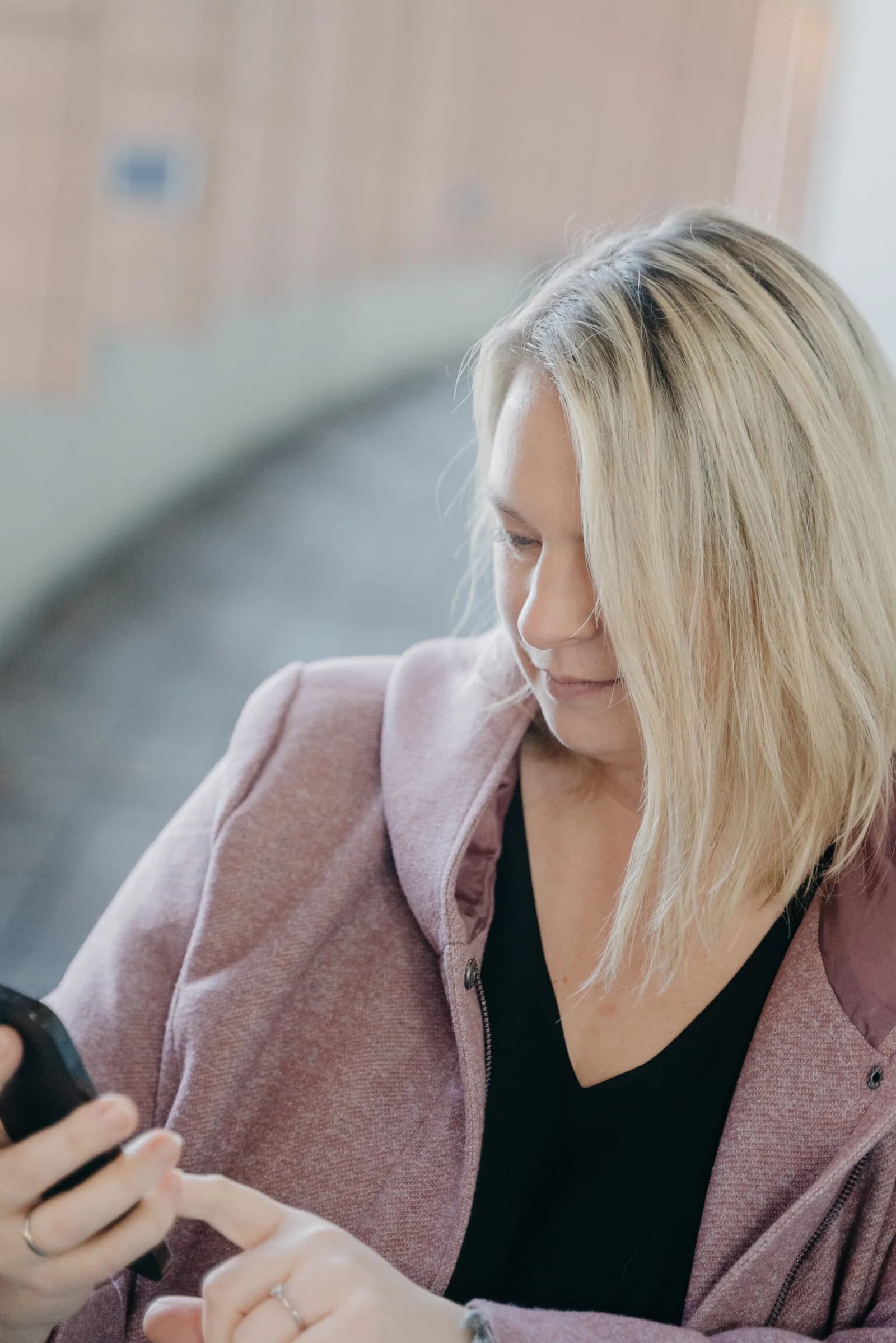 Eva Czaja in rosa Jacke schaut lächelnd auf ihr Smartphone