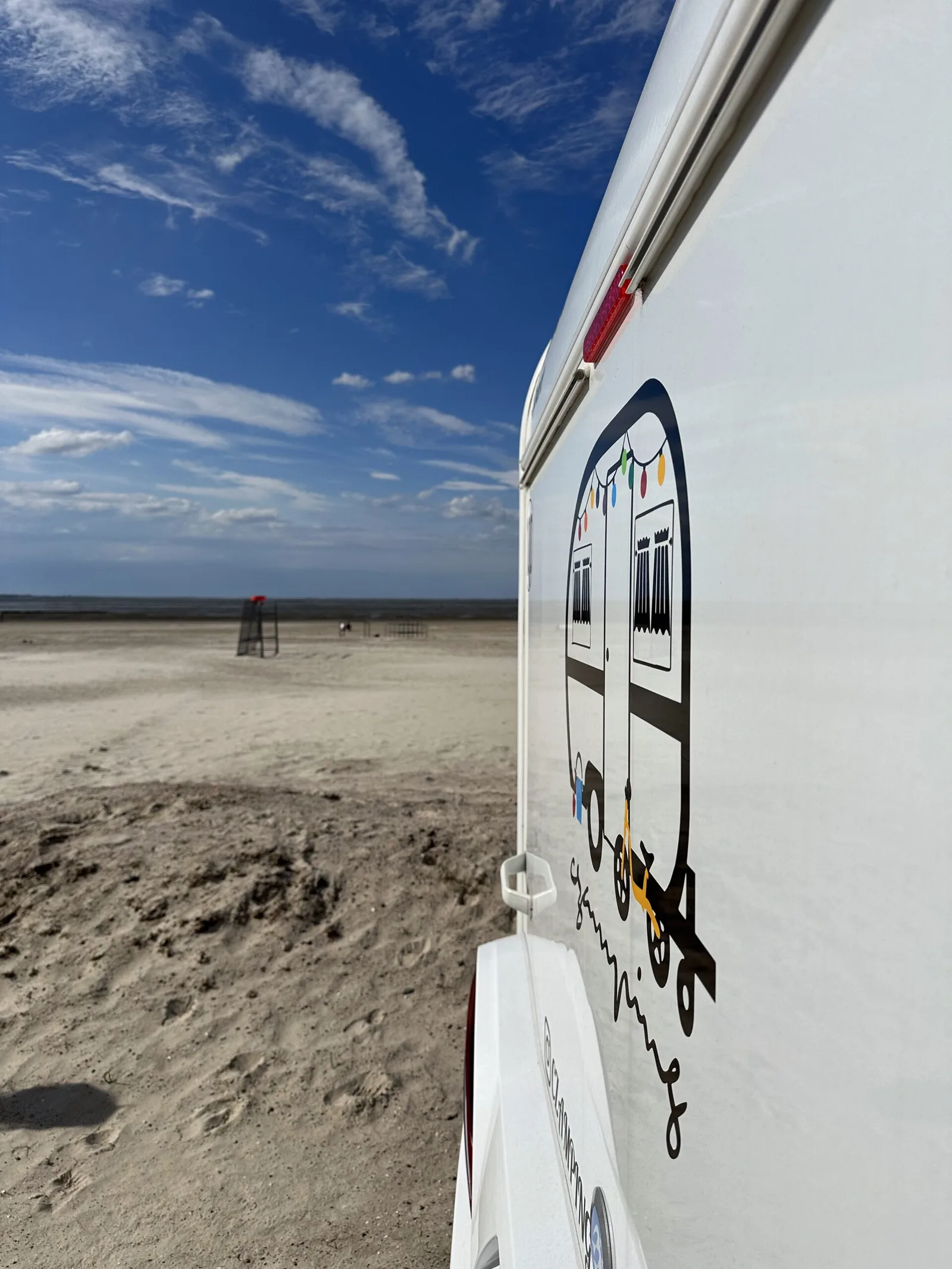 Wohnwagen mit Czamping-Beklebung am weiten Sandstrand unter blauem Himmel